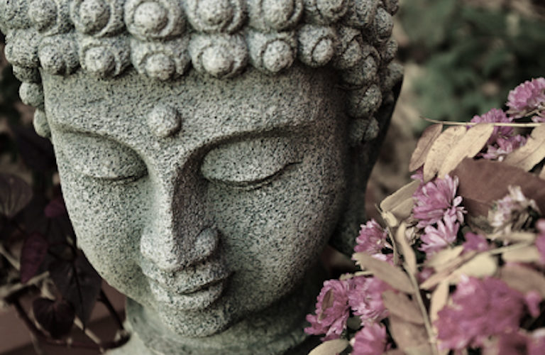 A bowed head of Buddha, with dried flowers nearby