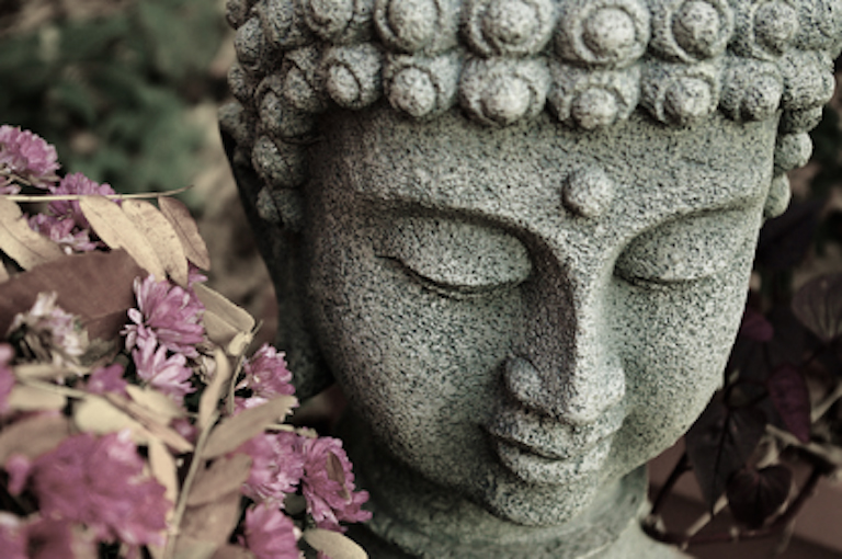 A bowed head of Buddha, with dried flowers nearby